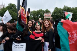 Image shows three Afghan women holding Afghan flags at a protest